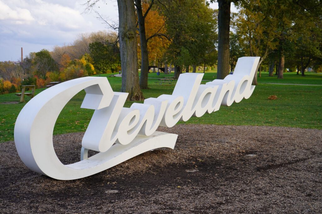 Large white cursive script sign reading Cleveland in a green park setting, perfect to include in a greenville trip planner comparison.